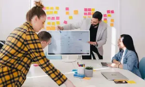 Equipo colaborando en ideas para los mejores negocios online. Un hombre señala la pantalla de un ordenador, mientras otros dos observan.