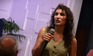 Mujer con micrófono, vestida de verde, parece hablar con pasión, casi al punto de morir de éxito.
