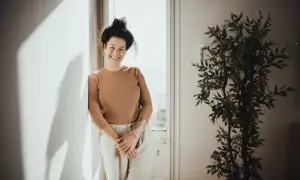 Mujer sonriente apoya en pared, con planta y luz. Sus youtoproject opiniones son positivas.