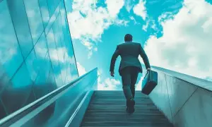 Hombre con maletín subiendo escaleras hacia el cielo azul, simbolizando un modelo de negocio escalable y el éxito.