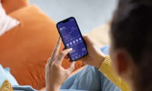 Persona revisa su teléfono móvil, mostrando una gráfica de inversión y opciones para la compra de acciones.