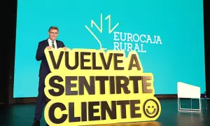 Hombre sonriente con traje sostiene cartel amarillo con mensaje "Vuelve a sentirte cliente" y logo de Eurocaja Rural.
