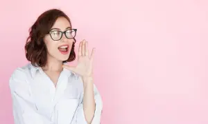 Mujer con gafas y camisa blanca, con la mano en la boca, como si estuviera contando secretos o dando noticias sobre entrevistas a emprendedores.