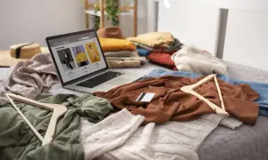 Un portátil muestra una tienda de moda online rodeado de ropa y perchas, ideal para vender ropa desde casa.