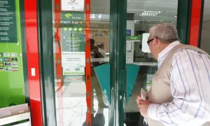 Un hombre mira la entrada de una sucursal de Unicaja, preguntándose qué bancos adelantan las pensiones este mes.
