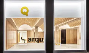 Interior de una oficina de arquitectos con paredes de madera, techo curvo y el logo "Q" en amarillo.