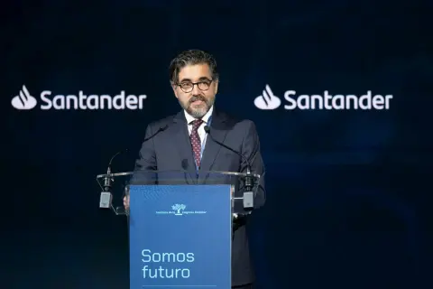 Hombre con traje habla en un congreso. El logo de Santander aparece dos veces. Opiniones sobre Banco Santander.