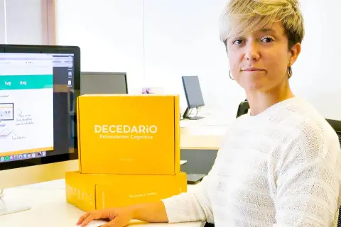 Diana de Arias, rodeada de cajas de "Decedario", un juego para estimulación cognitiva.