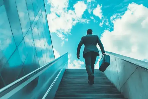 Hombre con maletín subiendo escaleras hacia el cielo azul, simbolizando un modelo de negocio escalable y el éxito.