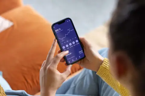 Persona revisa su teléfono móvil, mostrando una gráfica de inversión y opciones para la compra de acciones.