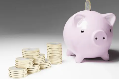 Cerdo rosa con monedas apiladas, simbolizando el inicio de emprender sin dinero y el ahorro para un futuro próspero.