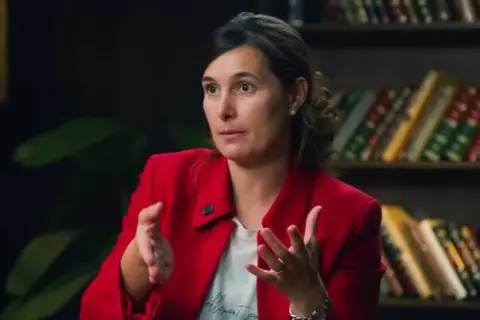 Andrea, del club de inversión, comparte sus opiniones con gestos enfáticos. Detrás, estanterías llenas de libros.
