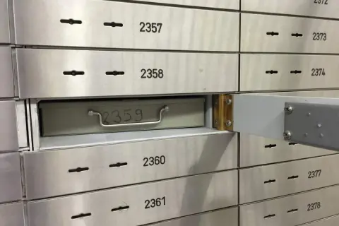 Una fila de casilleros de seguridad de banco. El casillero 2359 está parcialmente abierto, mostrando una caja metálica con un asa.