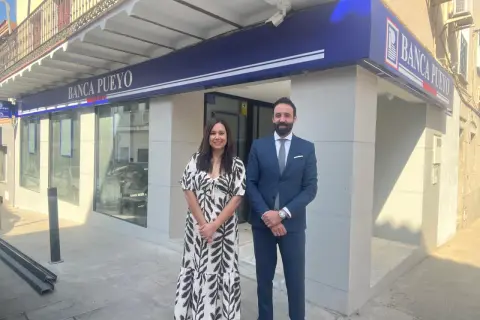 Dos empleados sonríen frente a la sucursal de Banca Pueyo. Las opiniones sobre Banca Pueyo son positivas.