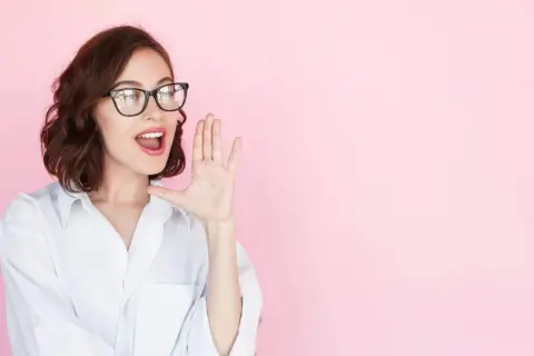 Mujer con gafas y camisa blanca, con la mano en la boca, como si estuviera contando secretos o dando noticias sobre entrevistas a emprendedores.