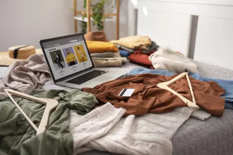 Un portátil muestra una tienda de moda online rodeado de ropa y perchas, ideal para vender ropa desde casa.