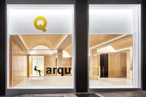 Interior de una oficina de arquitectos con paredes de madera, techo curvo y el logo "Q" en amarillo.