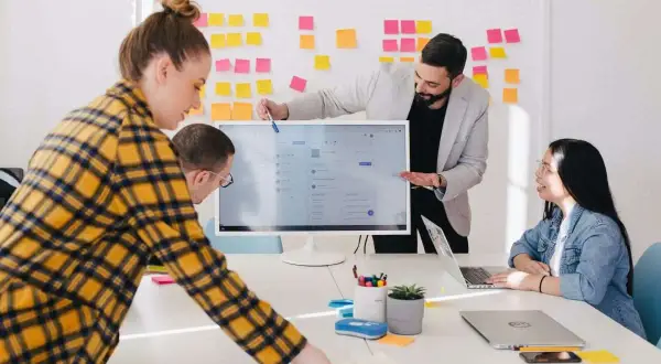 Equipo colaborando en ideas para los mejores negocios online. Un hombre señala la pantalla de un ordenador, mientras otros dos observan.