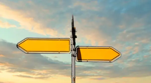 Doble señalización amarilla vacía, como **leading indicators** de un camino a seguir, contra un cielo nublado.