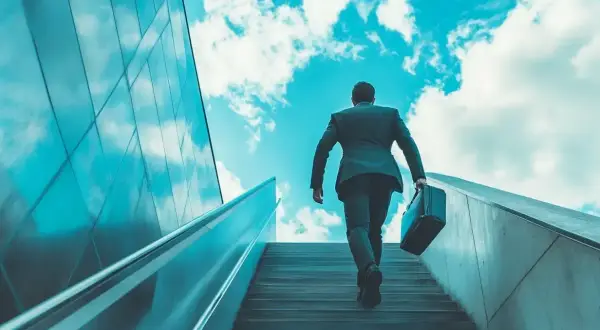 Hombre con maletín subiendo escaleras hacia el cielo azul, simbolizando un modelo de negocio escalable y el éxito.