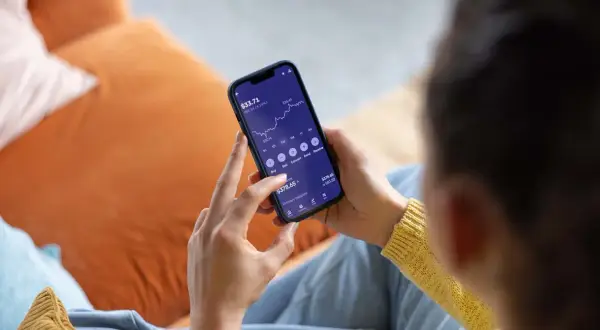 Persona revisa su teléfono móvil, mostrando una gráfica de inversión y opciones para la compra de acciones.