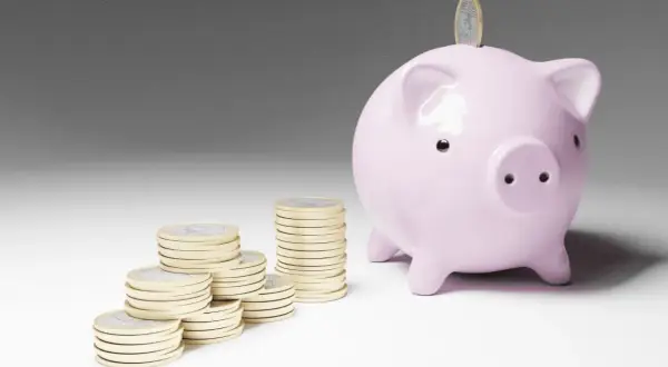 Cerdo rosa con monedas apiladas, simbolizando el inicio de emprender sin dinero y el ahorro para un futuro próspero.