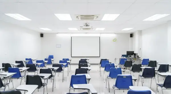 Aula vacía con sillas azules y negras, mesas y proyector. Ideal para pensar en los requisitos para abrir una academia de formación no reglada.