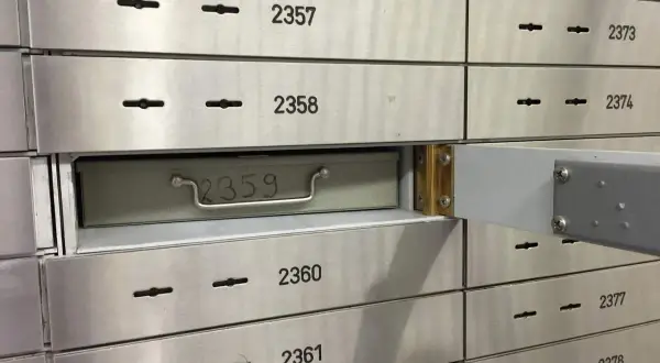 Una fila de casilleros de seguridad de banco. El casillero 2359 está parcialmente abierto, mostrando una caja metálica con un asa.