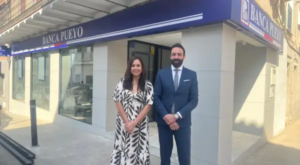 Dos empleados sonríen frente a la sucursal de Banca Pueyo. Las opiniones sobre Banca Pueyo son positivas.