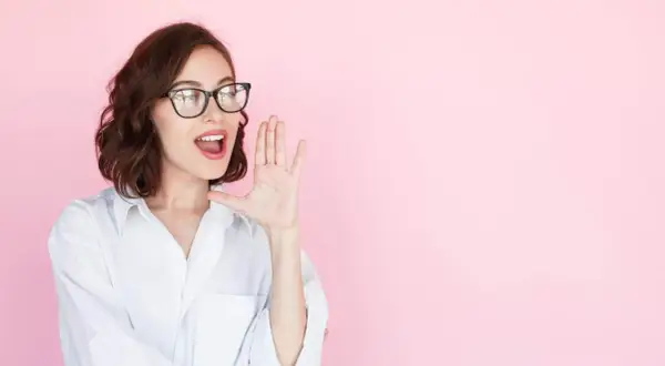 Mujer con gafas y camisa blanca, con la mano en la boca, como si estuviera contando secretos o dando noticias sobre entrevistas a emprendedores.