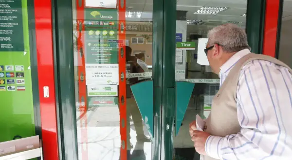 Un hombre mira la entrada de una sucursal de Unicaja, preguntándose qué bancos adelantan las pensiones este mes.