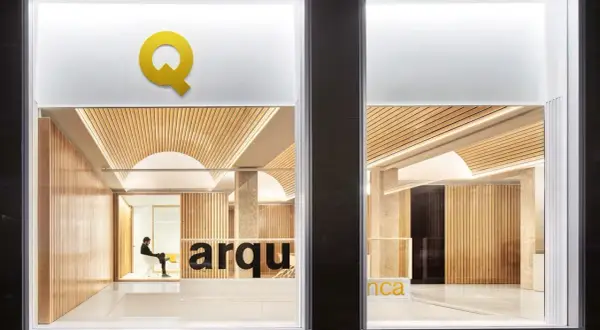Interior de una oficina de arquitectos con paredes de madera, techo curvo y el logo "Q" en amarillo.