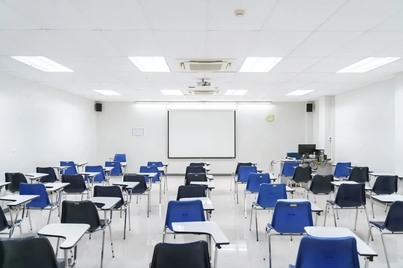 Aula vacía con sillas azules y negras, mesas y proyector. Ideal para pensar en los requisitos para abrir una academia de formación no reglada.