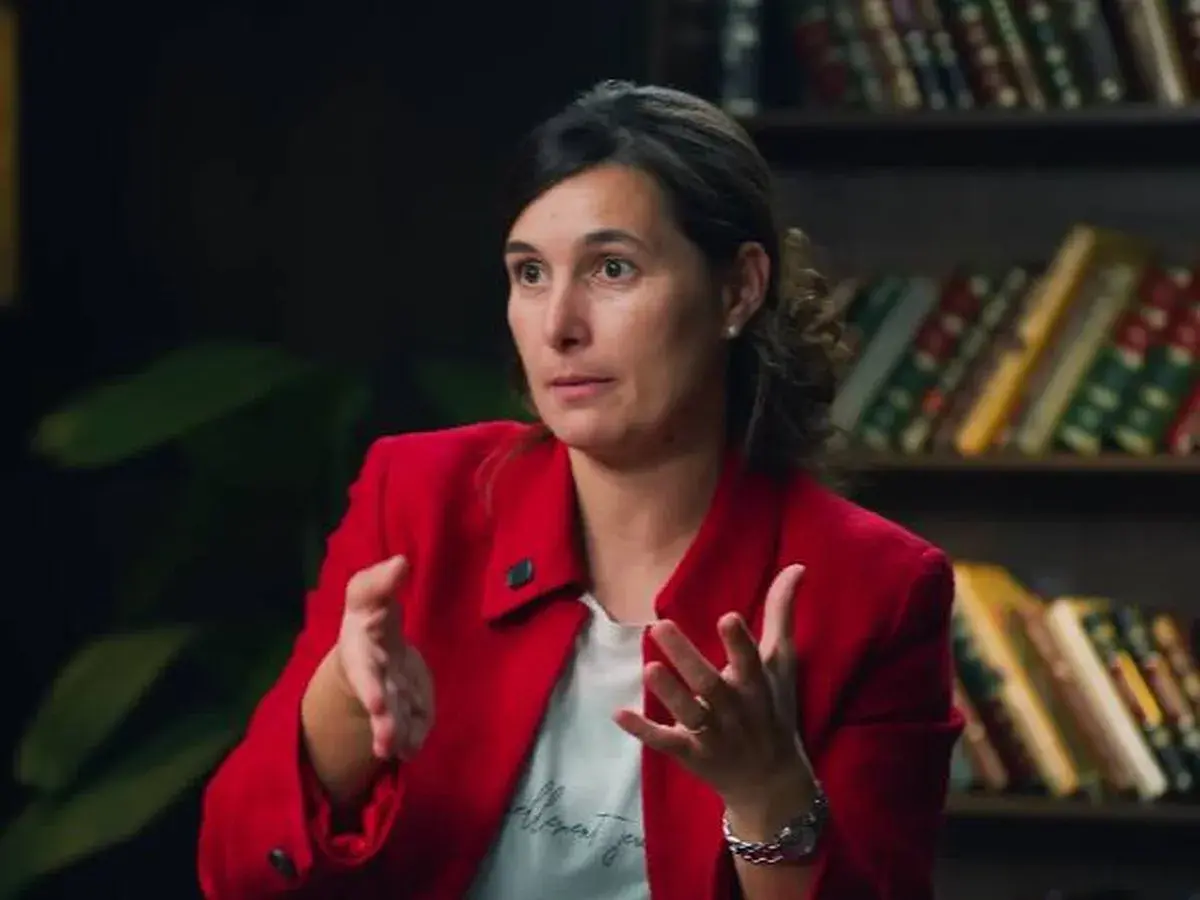 Andrea, del club de inversión, comparte sus opiniones con gestos enfáticos. Detrás, estanterías llenas de libros.
