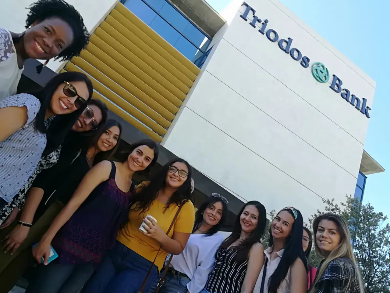Grupo de amigas sonriendo frente al edificio de Triodos Bank. Sus opiniones sobre el banco son positivas.