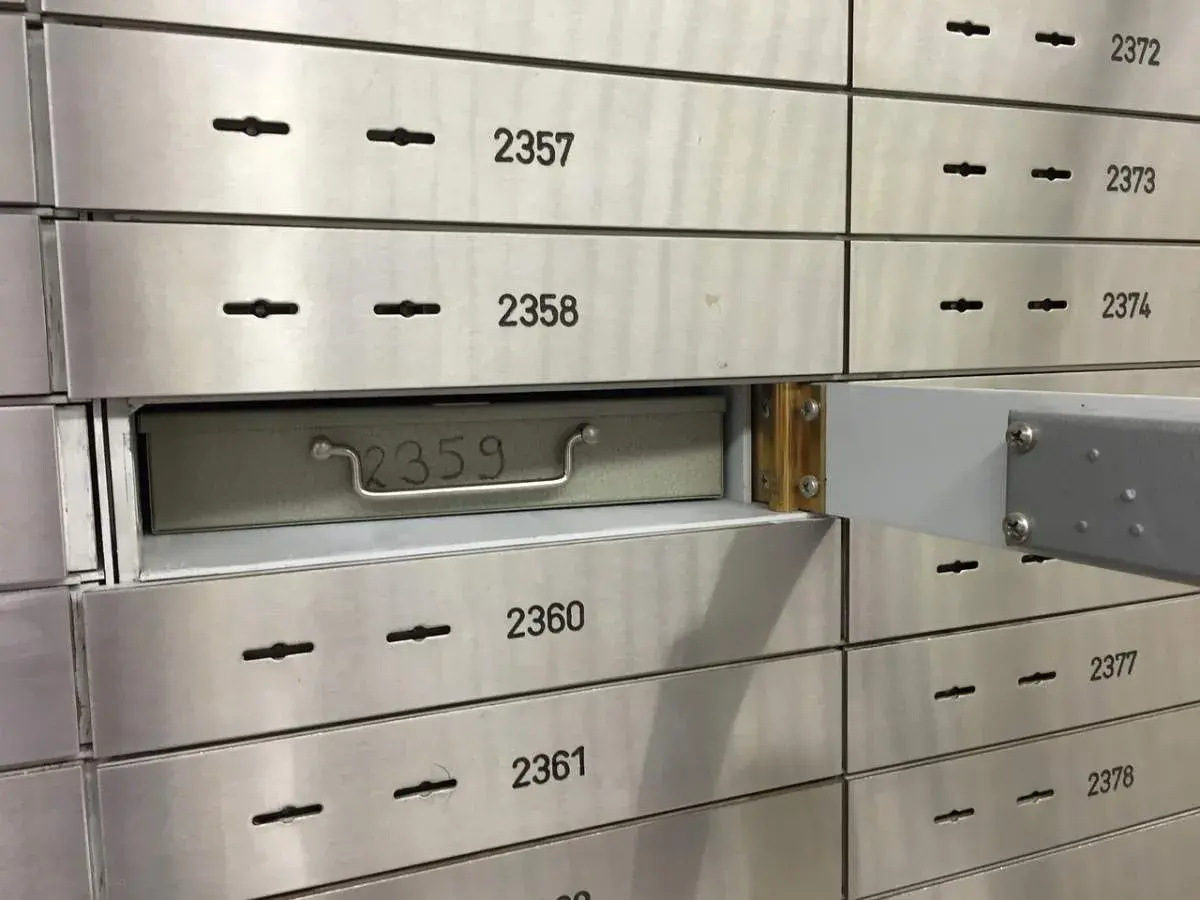 Una fila de casilleros de seguridad de banco. El casillero 2359 está parcialmente abierto, mostrando una caja metálica con un asa.