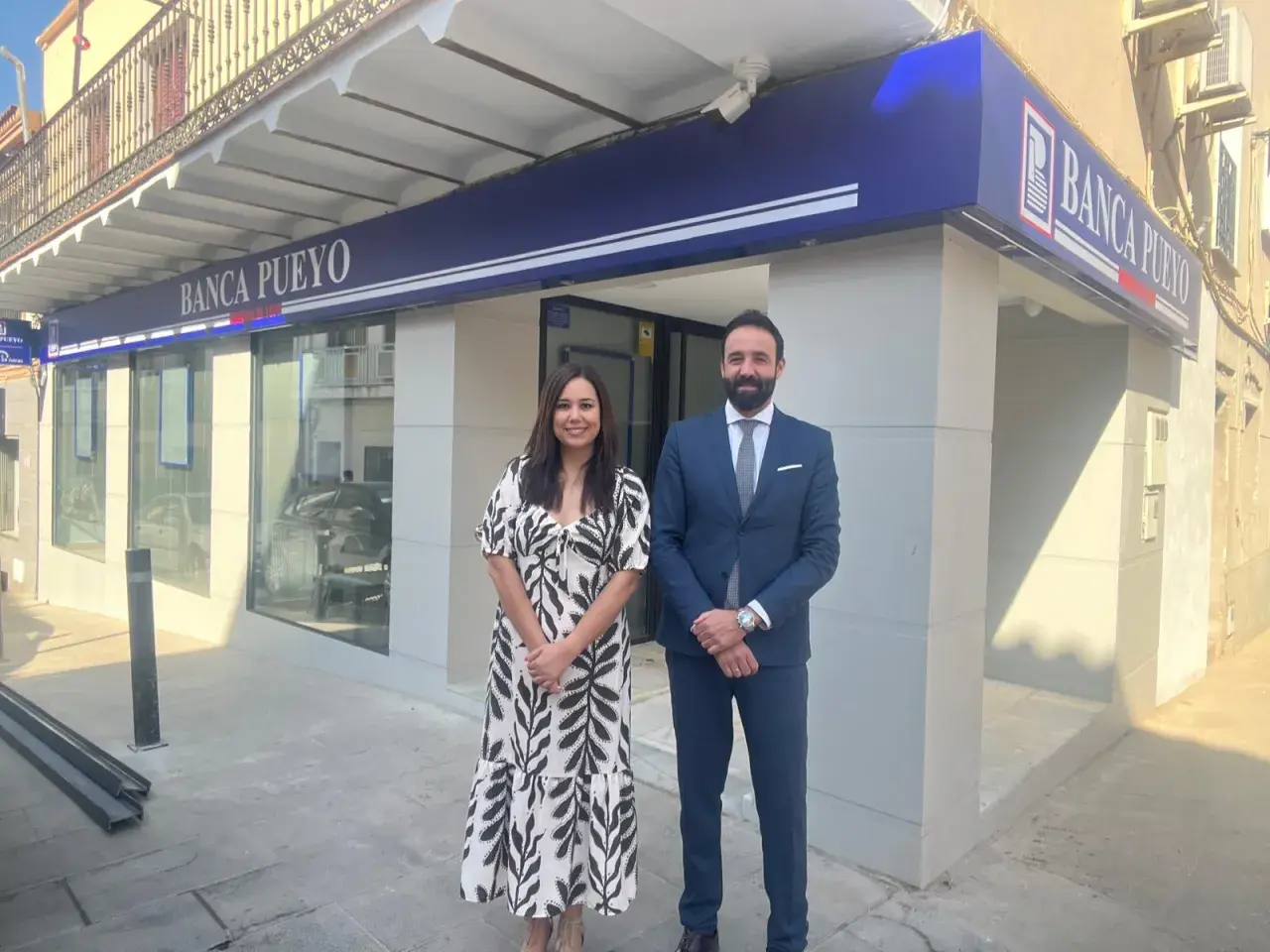 Dos empleados sonríen frente a la sucursal de Banca Pueyo. Las opiniones sobre Banca Pueyo son positivas.