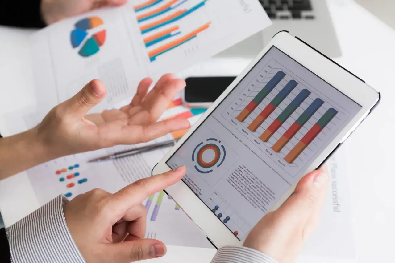Manos analizan gr&aacute;ficos en tablet y papeles, revisando los requisitos para crear empresa online.