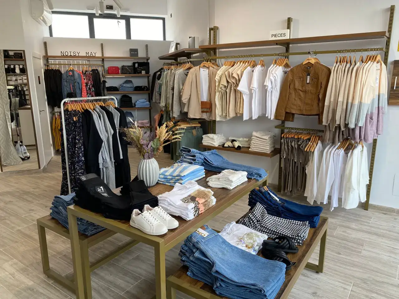 Interior de una tienda de ropa con percheros llenos de prendas y mesas con vaqueros y camisetas. &iexcl;Todo listo para abrir una tienda!