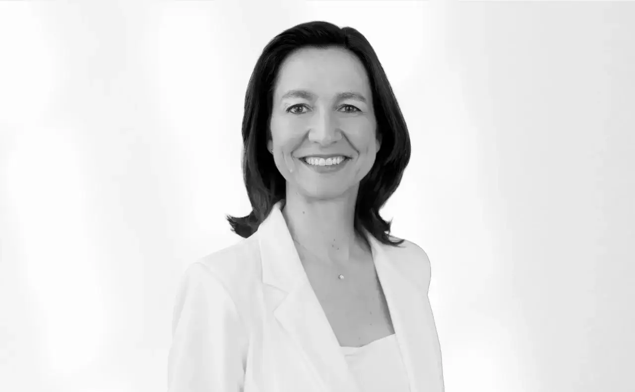 Helena Torras, una mujer sonriente con un blazer blanco, luce un collar delicado.