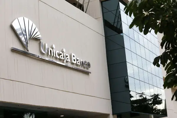 Fachada de Unicaja Banco con su logo metálico. Las reseñas sobre este banco son variadas, pero la imagen muestra su presencia física.