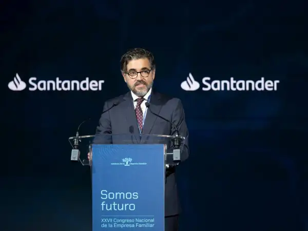 Hombre con traje habla en un congreso. El logo de Santander aparece dos veces. Opiniones sobre Banco Santander.