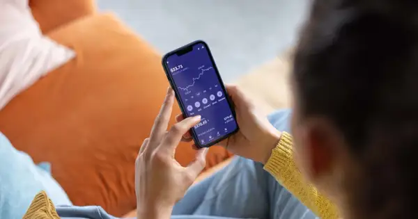 Persona revisa su teléfono móvil, mostrando una gráfica de inversión y opciones para la compra de acciones.