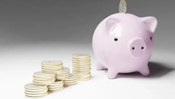 Cerdo rosa con monedas apiladas, simbolizando el inicio de emprender sin dinero y el ahorro para un futuro próspero.