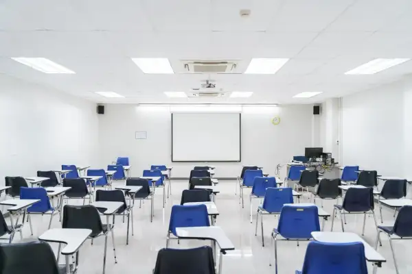 Aula vacía con sillas azules y negras, mesas y proyector. Ideal para pensar en los requisitos para abrir una academia de formación no reglada.