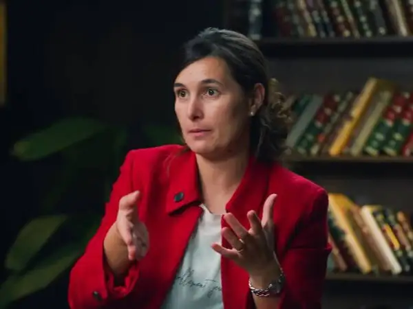 Andrea, del club de inversión, comparte sus opiniones con gestos enfáticos. Detrás, estanterías llenas de libros.