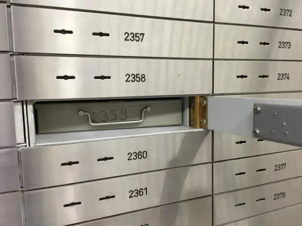 Una fila de casilleros de seguridad de banco. El casillero 2359 está parcialmente abierto, mostrando una caja metálica con un asa.