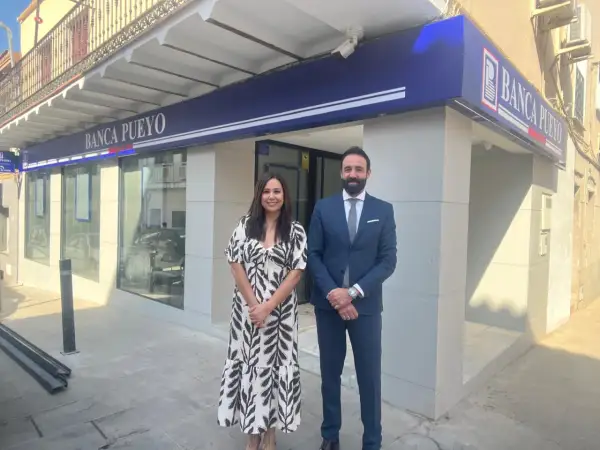 Dos empleados sonríen frente a la sucursal de Banca Pueyo. Las opiniones sobre Banca Pueyo son positivas.
