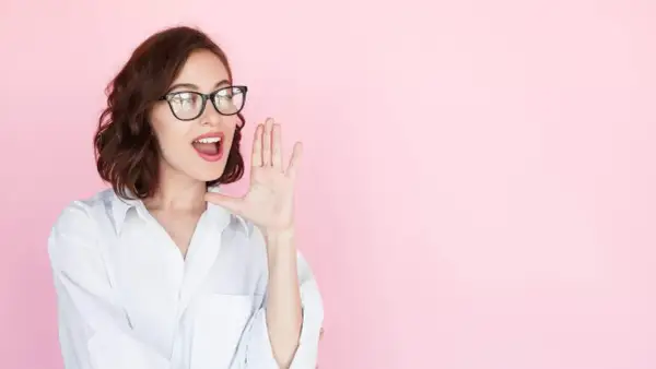 Mujer con gafas y camisa blanca, con la mano en la boca, como si estuviera contando secretos o dando noticias sobre entrevistas a emprendedores.