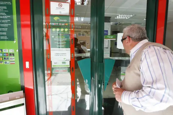 Un hombre mira la entrada de una sucursal de Unicaja, preguntándose qué bancos adelantan las pensiones este mes.